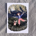 Postkarte Dancing in the Moonlight von Hannahs Firlefanz A6, Person tanzt nachts mit einem Dackel auf der Wiese unter Lichterketten