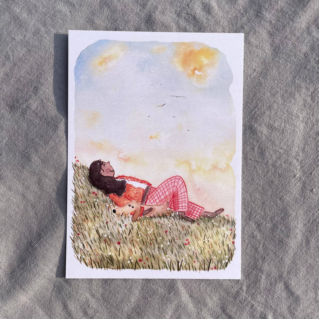 Postkarte Head in the Clouds von Hannahs Firlefanz A6, Person liegt mit Hund im Gras und schaut in den Sommerhimmel