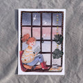 Postkarte Leseabend von Hannahs Firlefanz A6, Person mit roten Locken liest am Fenster, draußen fällt Schnee, daneben Tee und Bücher