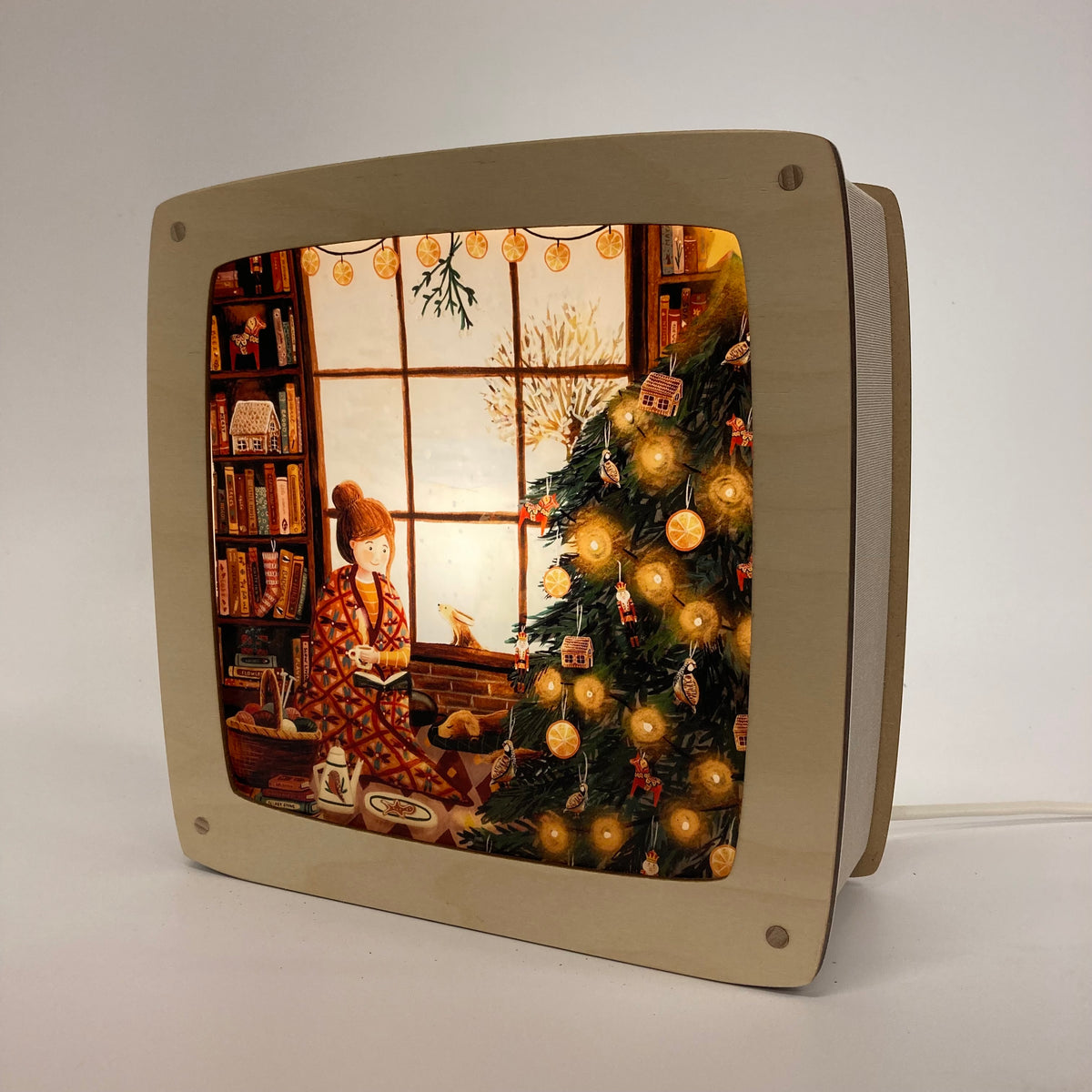 Motiv Kuscheln am Weihnachtsbaum von Esther Bennink für die magische Lampe: Lesende Person am Fenster neben einem leuchtenden Weihnachtsbaum und Bücherregal
