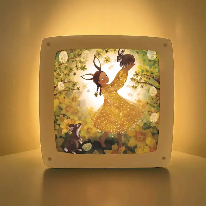 Motiv Osterhase von Bijdehansje für die magische Lampe: Kind mit Hasenohren tanzt in gelben Blumen, daneben ein Hase