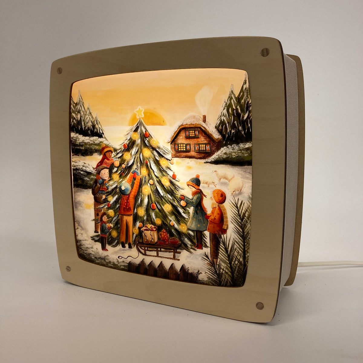 Motiv Weihnachtsbaum von Esther Bennink für die magische Lampe: Familie schmückt draußen im Schnee einen Weihnachtsbaum, dahinter ein Haus im Abendlicht