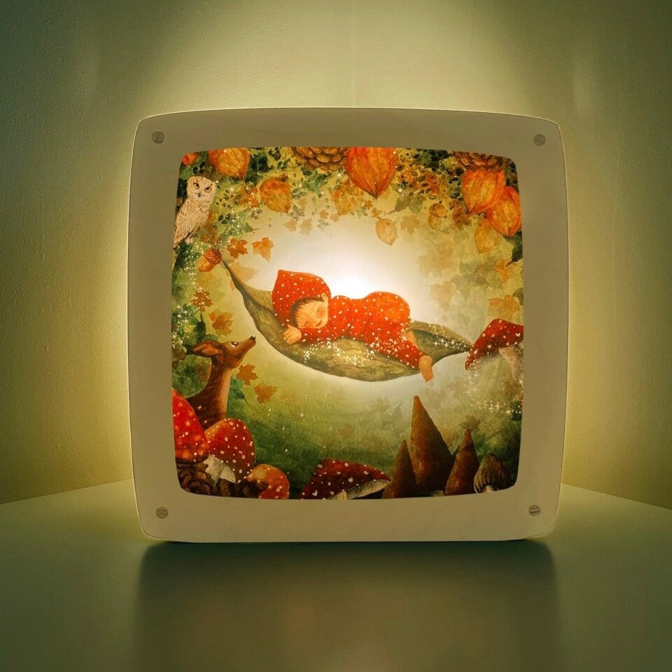 Motiv Zauberwald von Bijdehansje für die magische Lampe: Baby schläft in einer Hängematte aus Blättern zwischen Fliegenpilzen und Herbstlaub