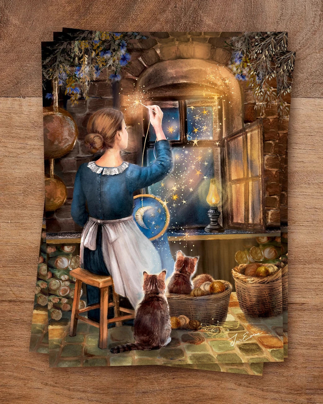Postkarte Die Näherin der Sterne von Iris Esther A6: eine Näherin sitzt am offenen Fenster ihres Steinhäuschens und stickt Sterne in den Nachthimmel, Katzen schauen zu