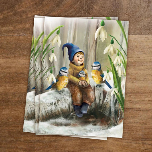 Postkarte Frühlingsankunft von Iris Esther A6: ein kleines Wichtelkind sitzt auf schmelzendem Schnee zwischen Blaumeisen und Schneeglöckchen