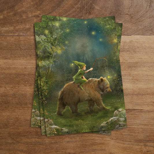 Postkarte Mitternachtsabenteuer von Iris Esther A6: ein kleines Wichtelkind reitet unter einem Sternenhimmel auf einem Bären durch den nächtlichen Wald