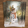 Postkarte Schneemann von Iris Esther A6: ein Schneemann mit zerknautschtem Hut und Karottennase, um ihn herum Rotkehlchen und Meisen im Schnee