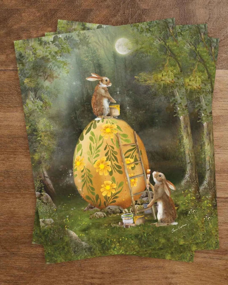 Postkarte Zusammenarbeit an Ostern von Iris Esther A6: zwei Hasen bemalen unter dem Frühlingsmond ein großes goldenes Ei mit Ringelblumen und Ranken
