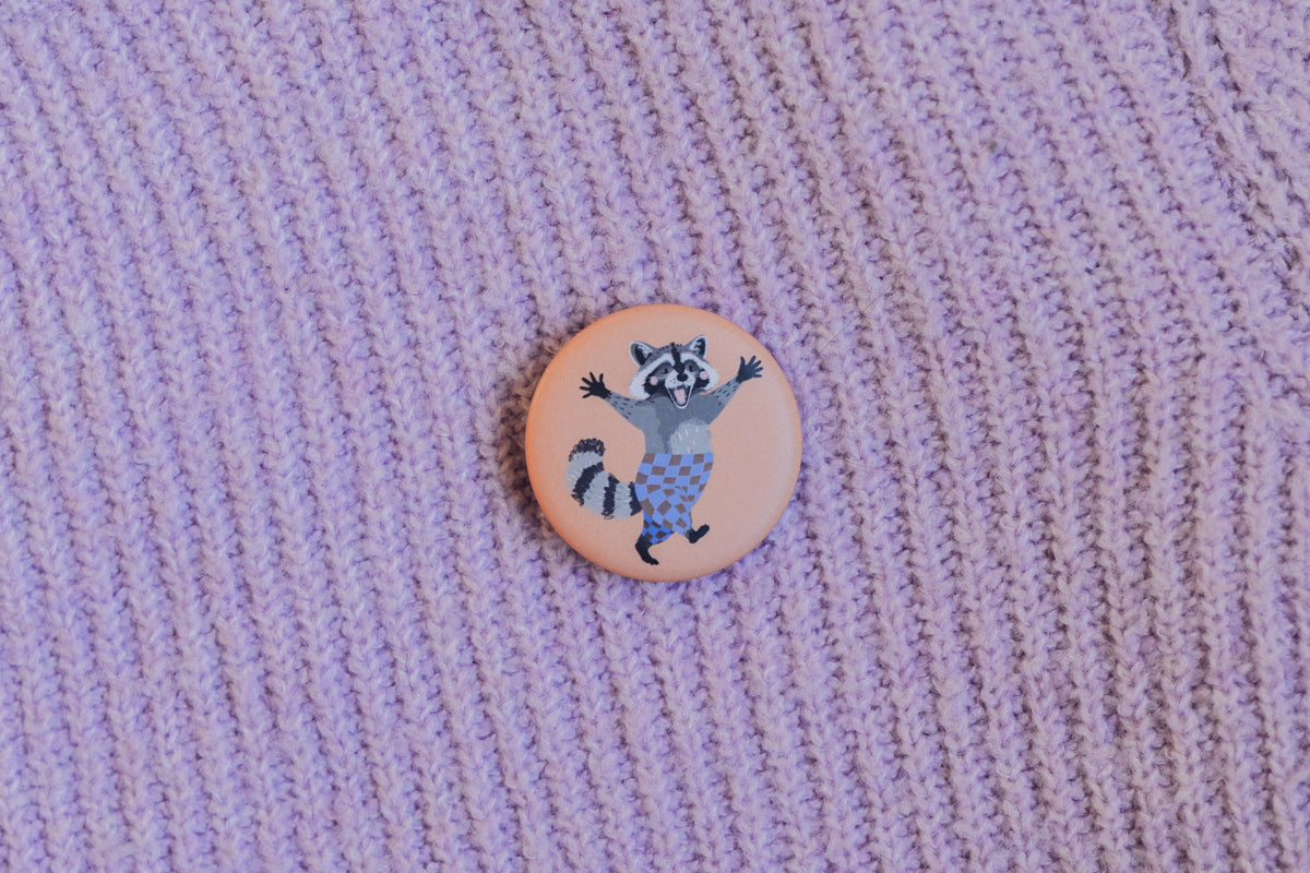 Button Waschbär von Liesels Wicht an einem lila Strickpullover angesteckt