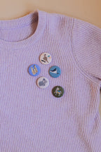 Button von Liesels Wicht am Ausschnitt eines lila Pullovers, Tragebeispiel
