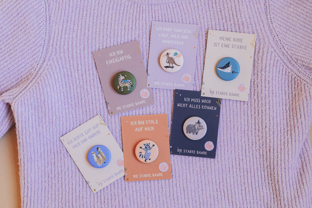 Buttons der starken Bande von Liesels Wicht auf ihren Kärtchen, auf einem lila Strickpullover ausgelegt