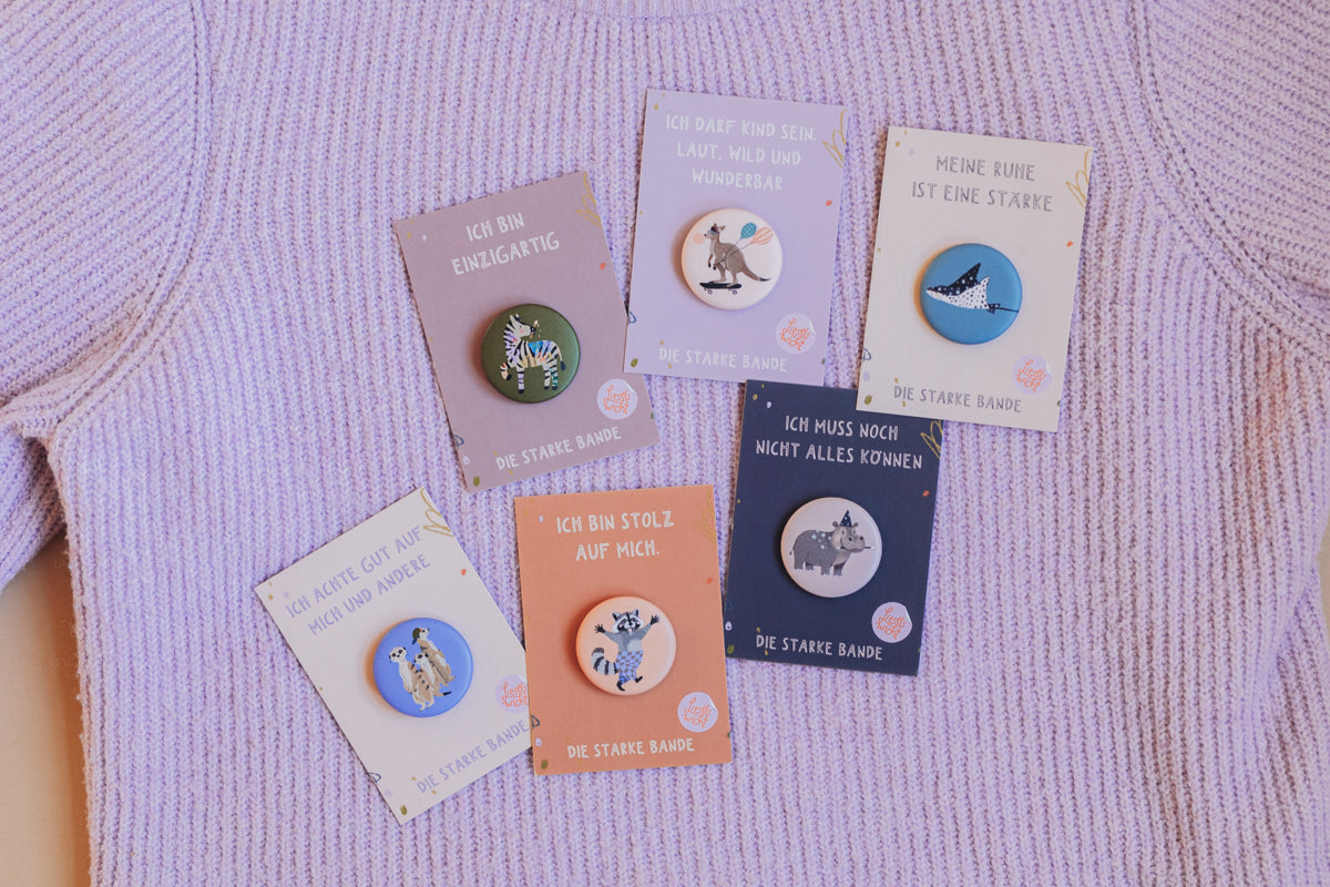 Buttons der starken Bande von Liesels Wicht auf ihren Kärtchen, auf einem lila Strickpullover ausgelegt