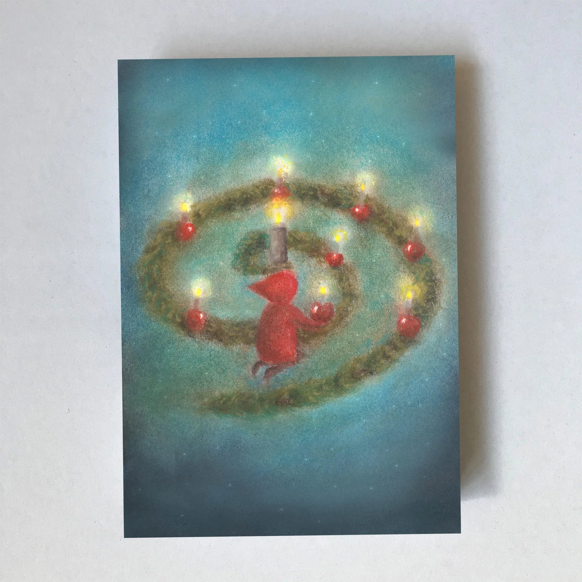 Postkarte Advent von Lot Bouwes A7: ein Wichtel sitzt in einer Adventsspirale aus Tannengrün mit leuchtenden Kerzen und roten Äpfeln