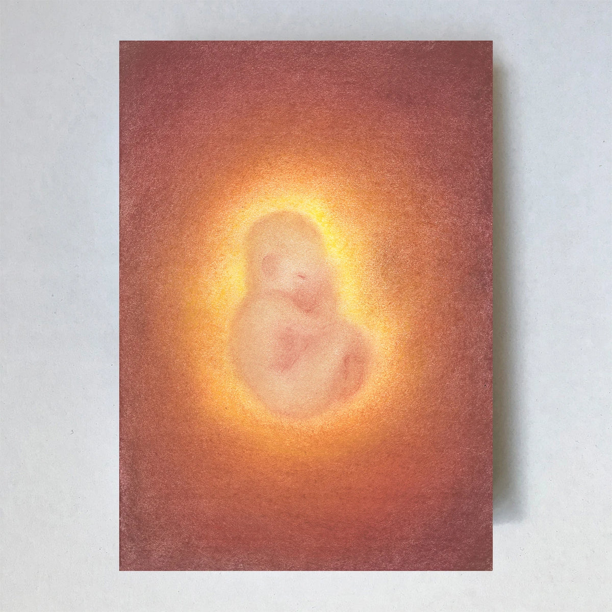 Postkarte Baby von Lot Bouwes A6: ein schlafendes Baby, eingerollt wie im Mutterleib, in einem warmen orange-goldenen Lichtkreis