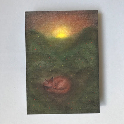 Postkarte Fuchs von Lot Bouwes A6: ein Fuchs schläft eingerollt auf einer grünen Lichtung, die Sonne geht hinter dem Wald unter