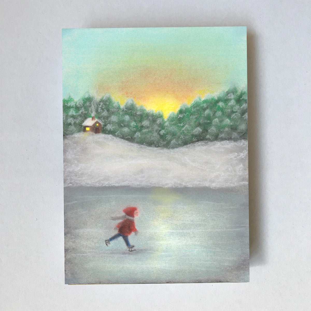 Postkarte Schlittschuh laufen von Lot Bouwes A6: ein Kind mit roter Mütze läuft Schlittschuh auf einem zugefrorenen See, dahinter verschneite Tannen, ein kleines rotes Haus und Abendrot