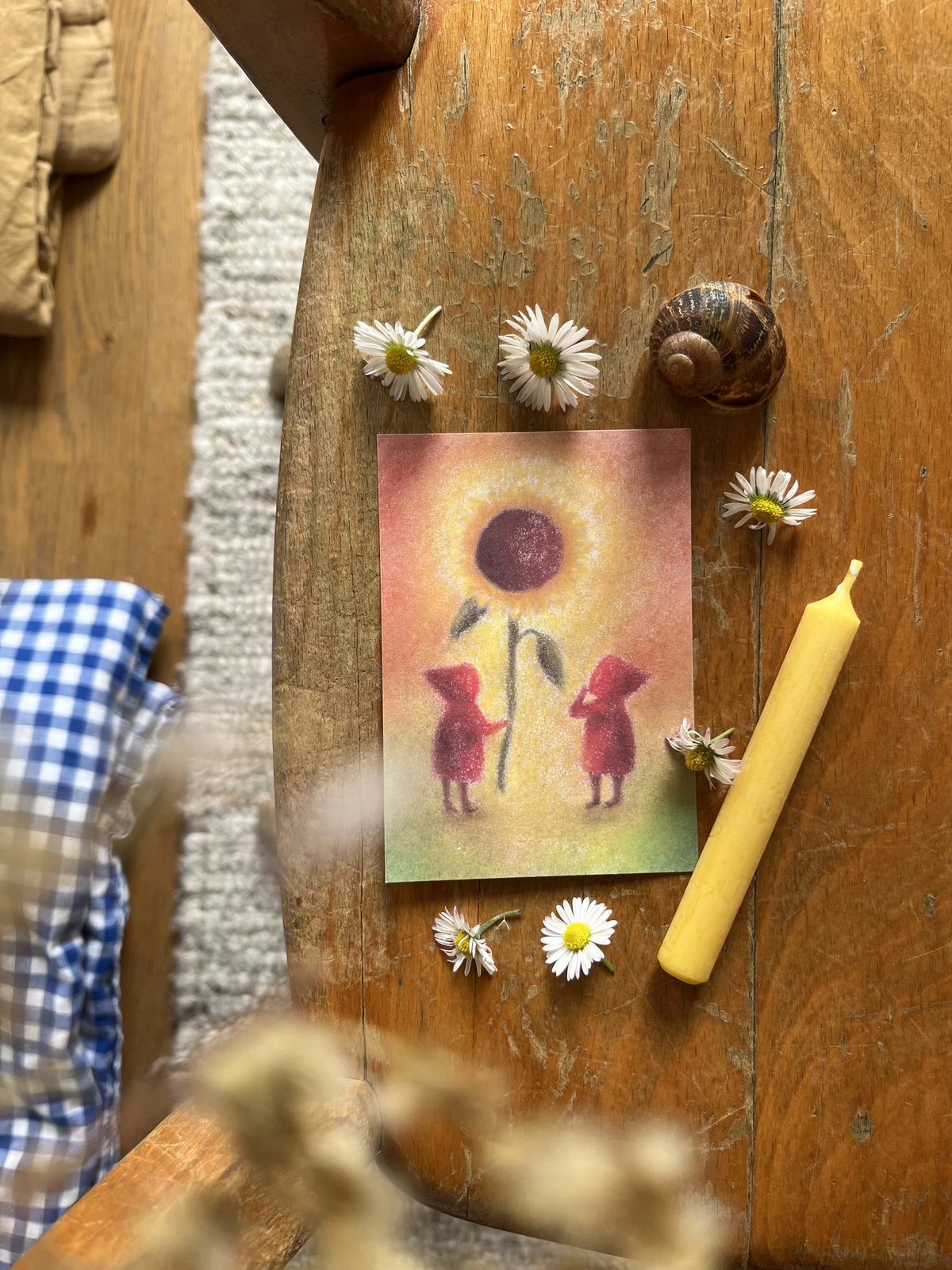 Postkarte Sonnenblume von Lot Bouwes A7 auf einem alten Holzstuhl mit Gänseblümchen, Schneckenhaus und Bienenwachskerze