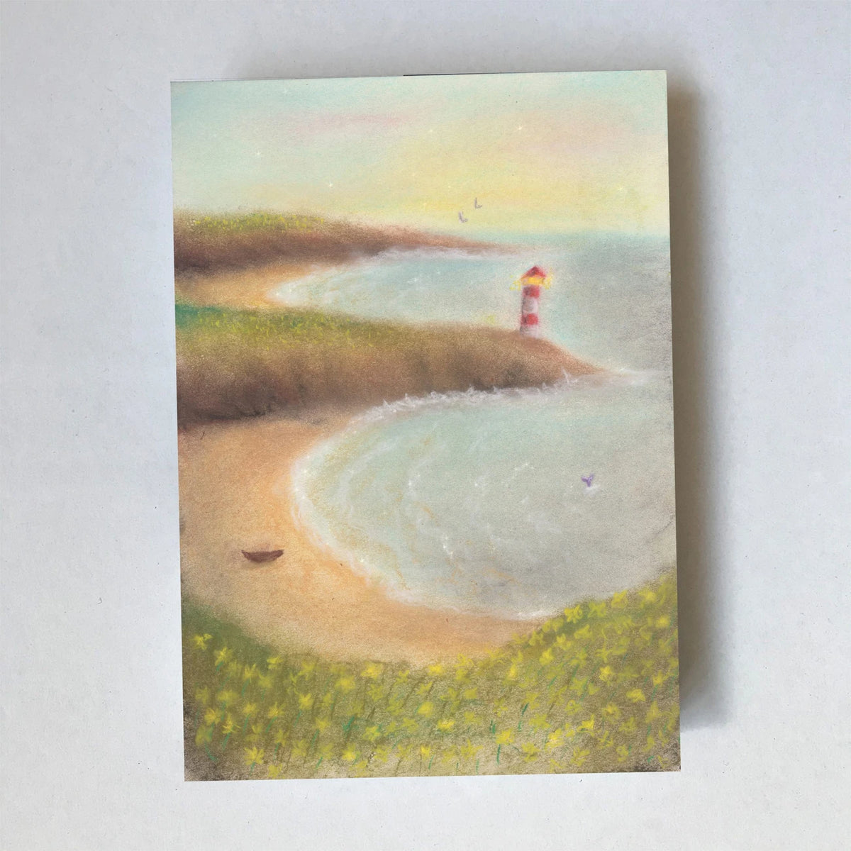 Postkarte Strand von Lot Bouwes A6: Küste mit Sandbucht, rot-weißer Leuchtturm auf der Landzunge, ein Boot am Strand, gelbe Blumen im Vordergrund