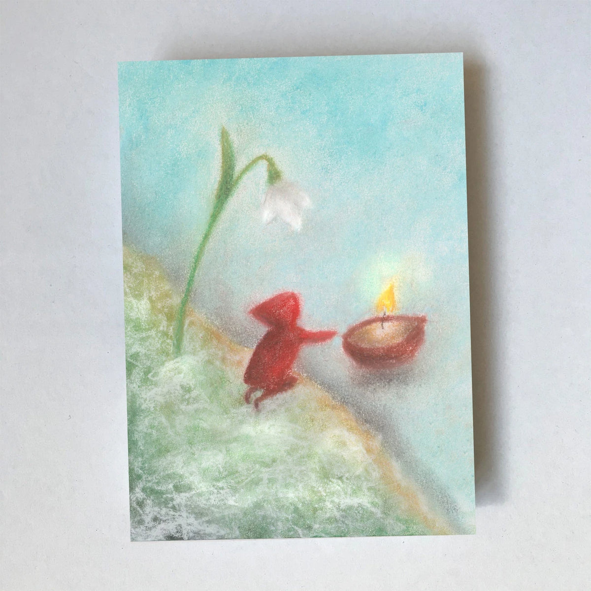 Postkarte Walnuss Kerze von Lot Bouwes A7: ein Wichtel schiebt ein Walnussschiffchen mit brennender Kerze übers Wasser, daneben ein Schneeglöckchen, hellblauer Himmel