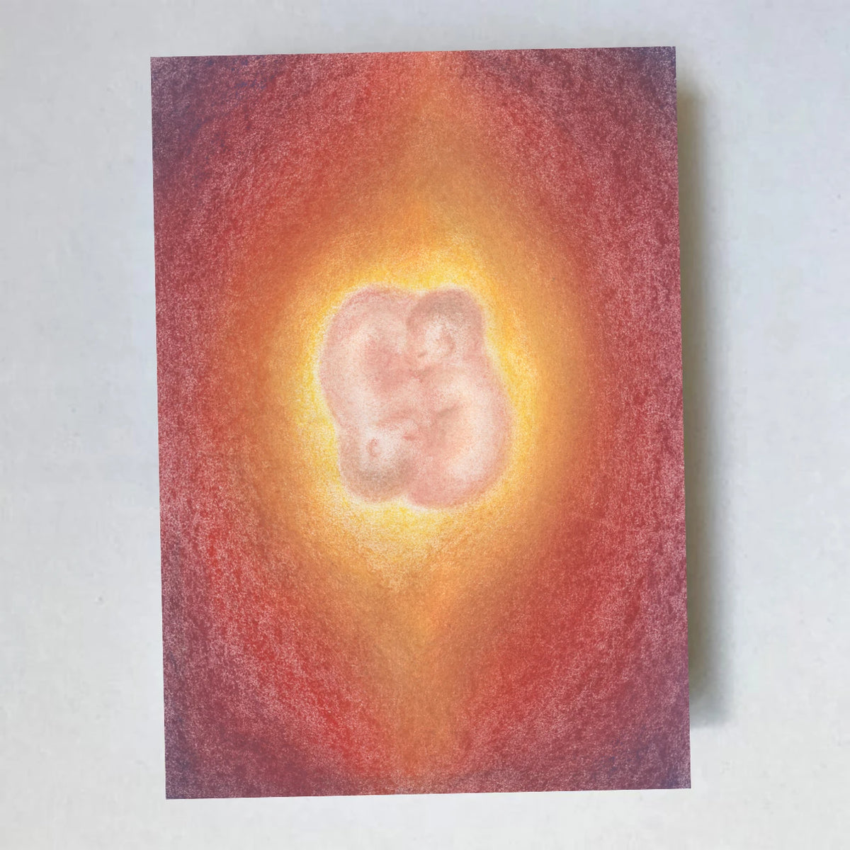 Postkarte Zwillinge von Lot Bouwes A6: zwei Babys kuscheln eng aneinander in einem warmen rot-orangen Lichtkreis