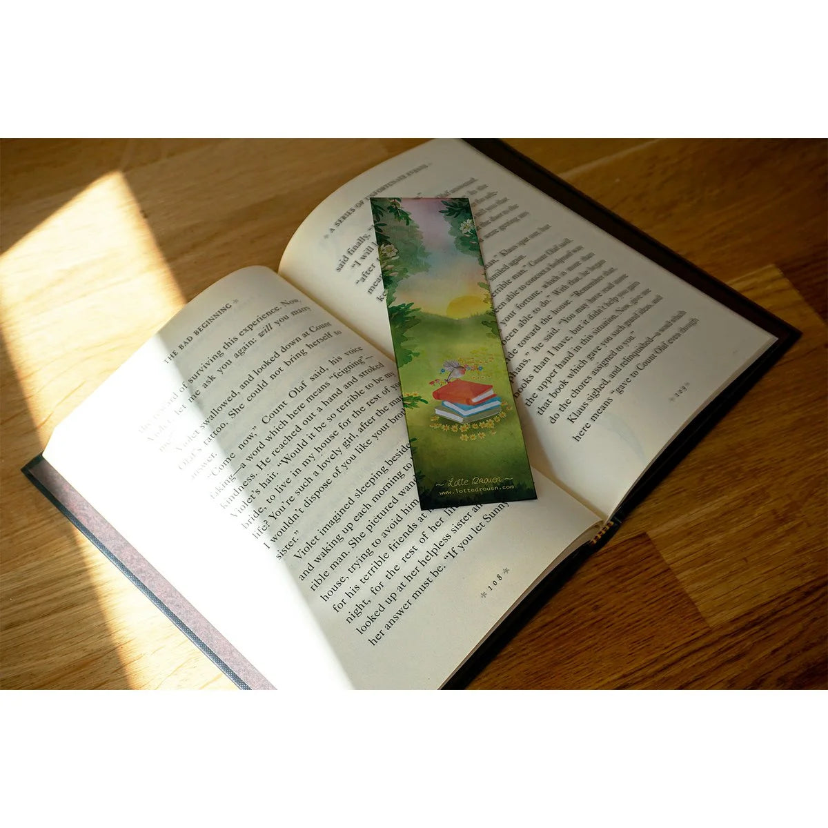 Lotte Drouen Lesezeichen Mit Liebe zum Buch, Vorderseite mit Vogel auf einem Bücherstapel in der Blumenwiese bei Sonnenuntergang, auf einem aufgeschlagenen Buch