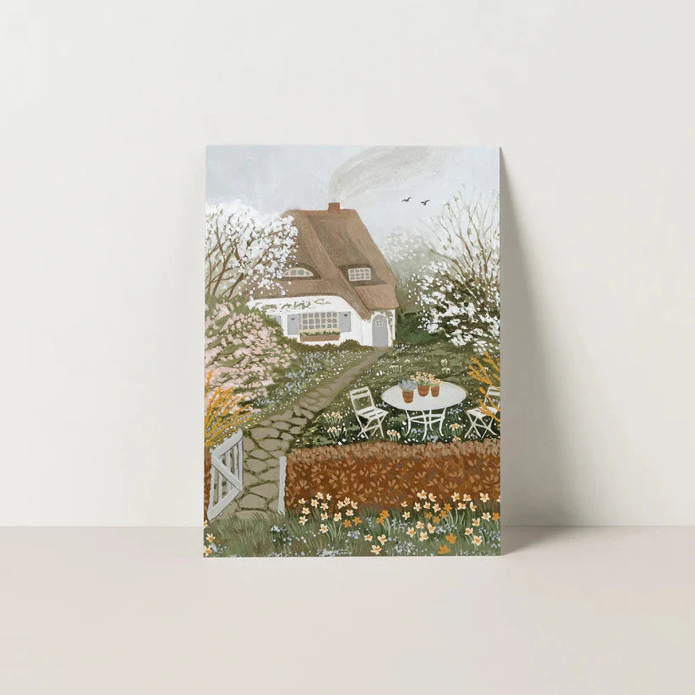 Postkarte Blühen von Robin Pieterse A6: ein weißes Reetdachhäuschen im Frühling zwischen blühenden Bäumen, ein Gartenweg führt zu einem Tisch mit zwei Stühlen