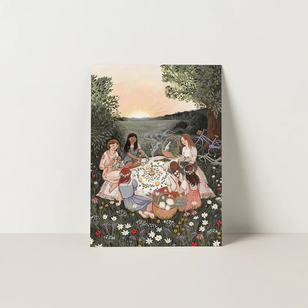 Postkarte Sommersonnenwende von Robin Pieterse A6: Freundinnen und Freunde flechten bei Sonnenuntergang auf einer Wildblumenwiese Blumenkränze und stoßen an