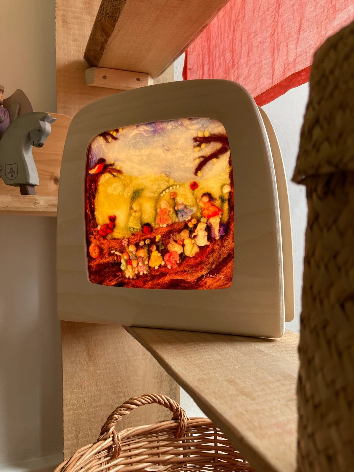 Magische Lampe Toverlux mit leuchtendem bunten Herbstmotiv im Holzregal über einem Weidenkorb