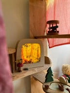 Magische Lampe Toverlux mit leuchtendem Herbstwald im Kinderzimmerregal, daneben Teddy und Holzspielzeug