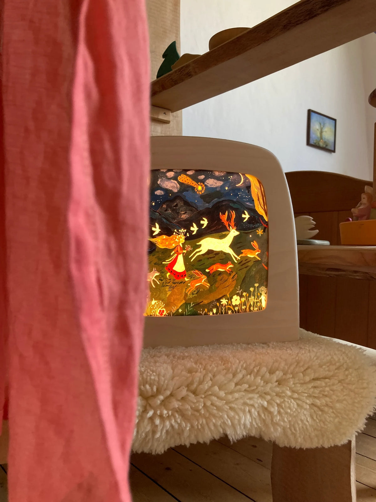 Magische Lampe Toverlux mit leuchtendem Nachtmotiv auf einem Schaffell, vorne ein rosa Tuch