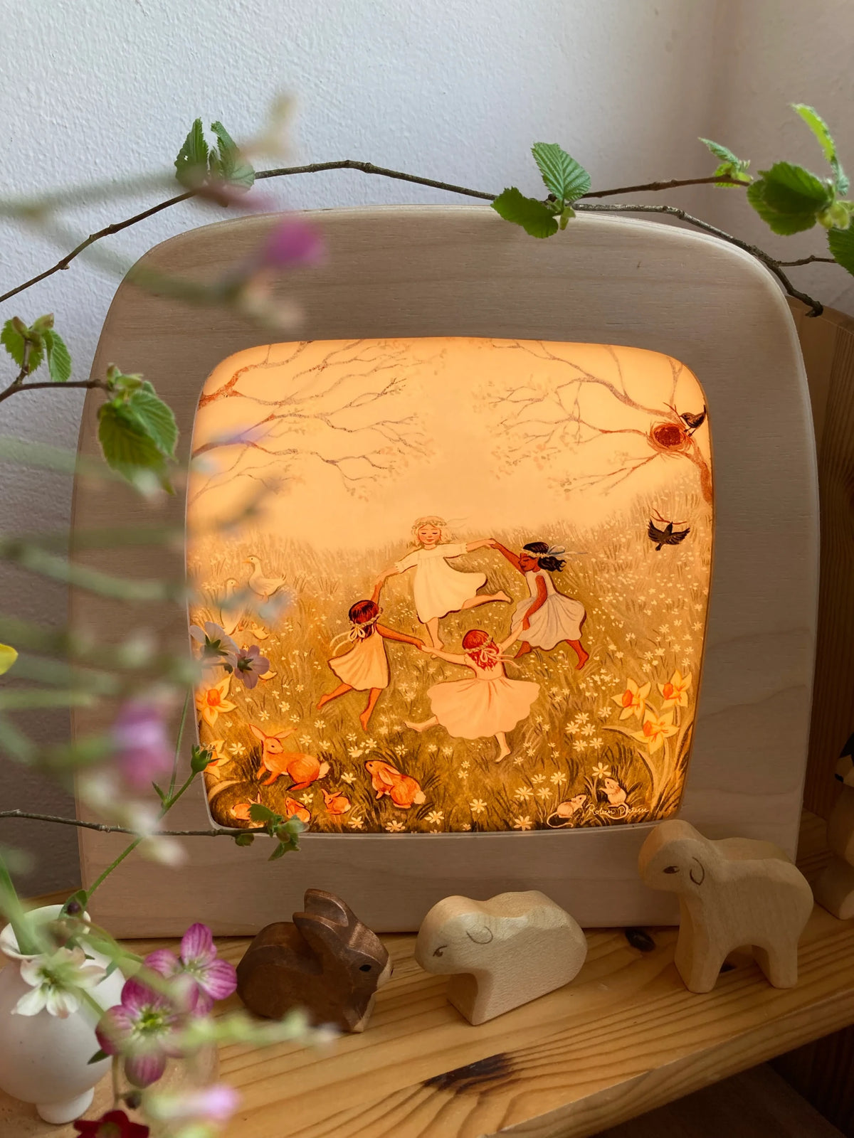 Toverlux Motiv Frühlingstanz von Robin Pieterse: Lampe mittig im Regal mit Frühlingszweig und Holzfiguren