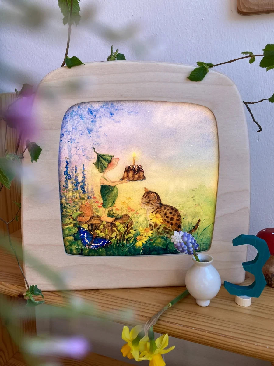 Toverlux Motiv Giesbert mit Kuchen von Daniela Drescher: leuchtende Lampe im Regal mit Narzissen und Holzpilzen