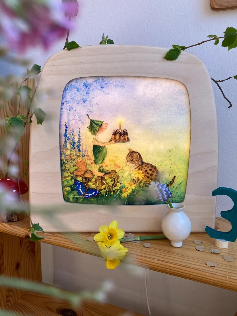Toverlux Motiv Giesbert mit Kuchen von Daniela Drescher: Lampe neben einer blauen Holzzahl Drei und Narzissen