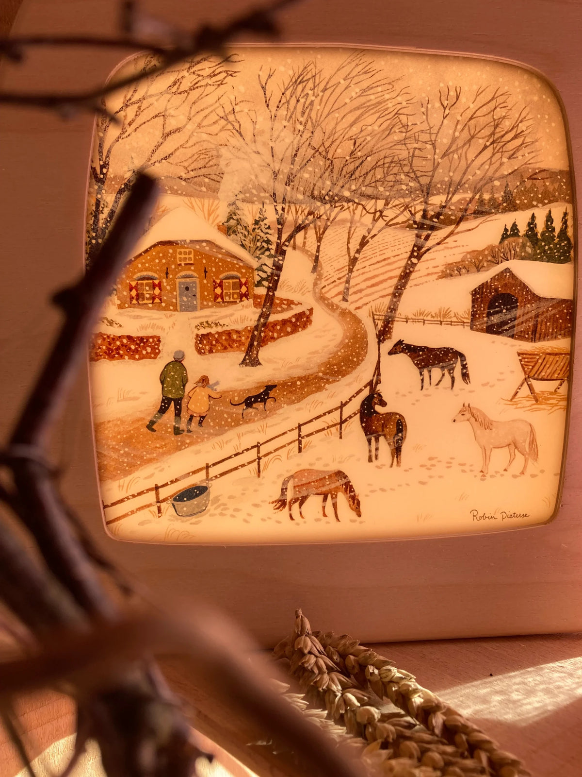 Toverlux Motiv Kältewelle von Robin Pieterse: leuchtende Lampe mit verschneitem Dorf und Pferden, davor Zweige