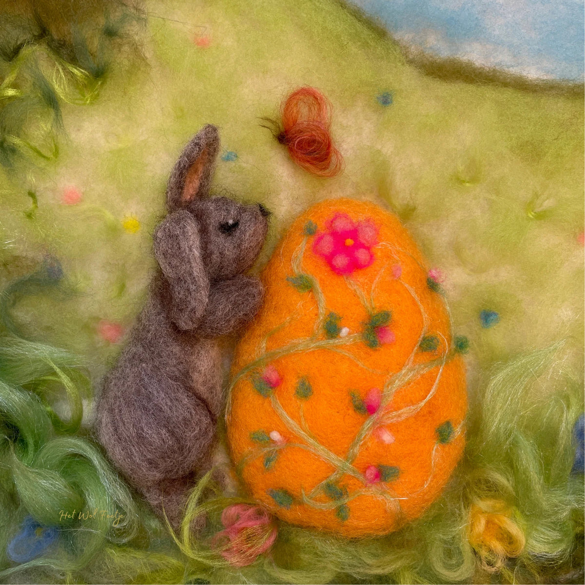 Toverlux Motiv Osterei von Het Wol Feetje, Illustration: Gefilzter Hase neben einem großen bunten Osterei auf der Wiese