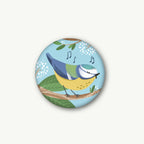 Magnet Blaumeise Blau von VIERUNDFÜNFZIG 37 mm, runder Magnet mit singender Blaumeise auf einem Zweig vor hellblauem Grund